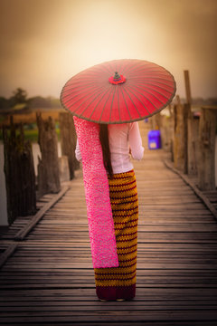 Woman Myanmar holding traditional red umbrella on U Bein wooden bridge during sunrise in Mandalay Myanmar.