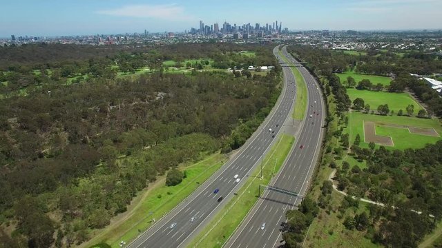 Slow aerial descend over cars driving on Eastern Freeway with Melbourne CBD skyline in the distance on bright summer day
