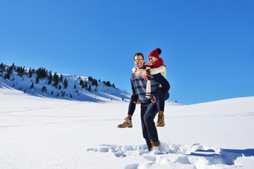 Fototapeta na wymiar Young couple having fun on snow. Happy man at the mountain giving piggyback ride to his smiling girlfriend.