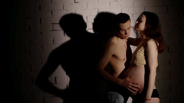 a young man gently stroking the belly of his pregnant girlfriend, the couple is standing near the wall