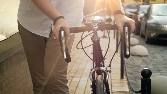 Closeup slow motion video of male hands holding vintage bicycle handles while walking on street at sunset