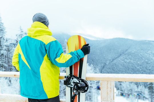 man stands with snowboard on the top of the hill