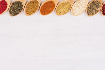 Assortment colorful powdered spices in bamboo spoons as decorative border. White wood background, top view, copy space.