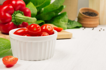 Healthy raw vegetables - cherry tomatoes, paprika, greens salad and pepper on soft white wood background, copy space.
