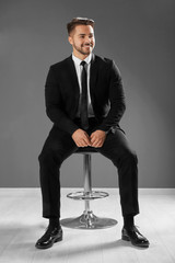 Handsome man in formal suit sitting on chair against grey wall