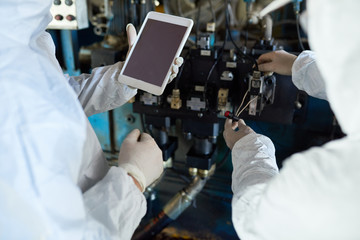 High angle close up of two factory workers wearing biohazard suits operating machine via digital tablet on modern processing plant