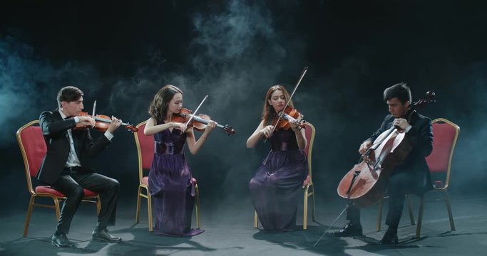 string musicians quartet during the performance of the symphony at the concert, black background with smoke