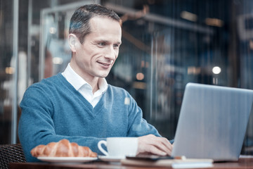 Online meeting. Kind male person looking forward while working with his laptop and going to drink coffee