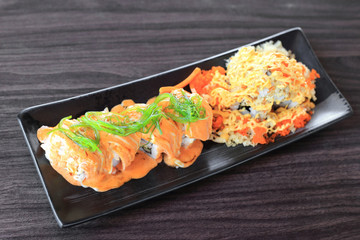 Maki sushi roll made of salmon top with wakame seaweed and special sushi top with crispy tempura flour, mayonnaise and flying fish roe - Japanese fusion food.
