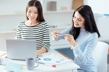 Successful startup. Charming smart creative female colleagues designing presentation while sitting at the table and taking photo of graphics 