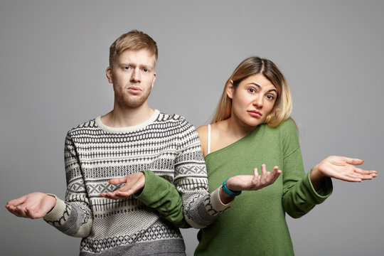 Picture of funny young couple man and woman having doubtful clueless looks, shrugging shoulders with open palms, feeling lost, looking at camera in confusion and uncertainty. Body language