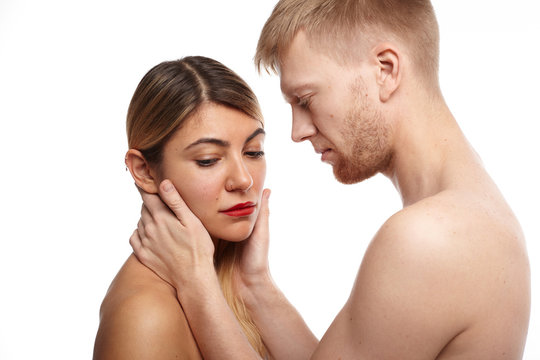 Intimate picture of adult couple male and female wearing no clothes in studio. Tender Caucasian partners making love: bearded man touching pretty face of shy blonde woman who is looking down