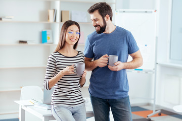 Coffee time. Happy emotional young couple talking while posing near the table and sipping coffee