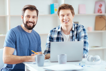 Wonderful work. Positive two male colleagues  smiling at the camera while planning strategy and posing on the blurred background