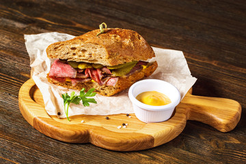 Closeup image of sandwich with meat and cucumbers at wooden board background.