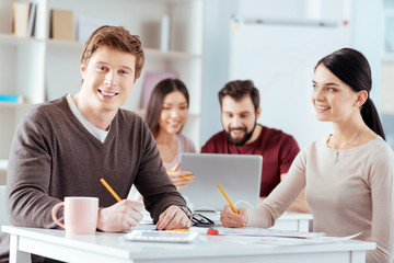  Love at work. Happy young two colleges holding pencils while working and woman admiring guy