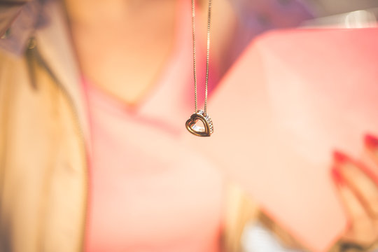 Young beautiful woman get a heart shape gold necklace gift from her boyfriend on Valentines Day. Closeup view.