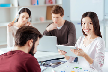 Obraz premium Devices at work. Happy cheerful young woman carrying tablet while smiling to the camera and making presentation