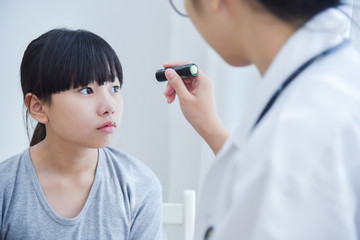 Doctor wear glasses checking a little girl patient eyes.
