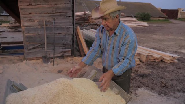 Old Farmer In A Cowboy Hat Shows Up And Picks Up The Wood Sawdust At A Sawmill