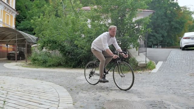 Slow motion footage of young bearded man riding vintage sport bicycle down the narrow street with paved road