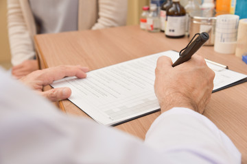 Asian male doctor is writing something on clipboard.