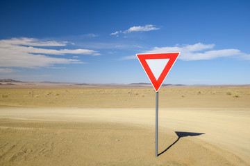 Wide angle view of a give way (yield) sign at a gravel road intersection in the Namibian Desert between Ai-Ais Fish River Canyon and Aussenkehr. Mountains in the background.