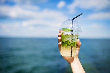 Recreation. Vacation. A refreshing cocktail. A trip to the sea. Female hand holds a cocktail or cold mojito against the sky and the sea