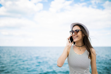 Beautiful young modern brunette woman in sunglasses talking on the phone with her friend on the beach against the sea