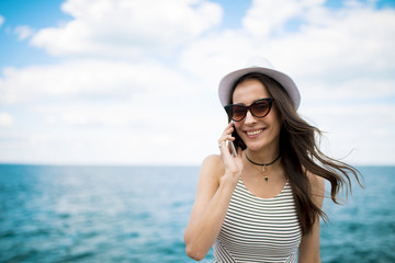 Attractive young smiling brunette woman in sunglasses talking on the phone on the beach against the sea