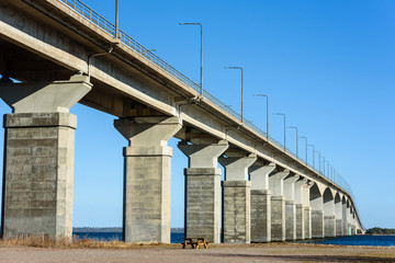 Empty bench under concrete bridge. Gray pillars support the weight of the structure. Vital part of infrastructure and link the island of Oland to mainland Sweden. © imfotograf