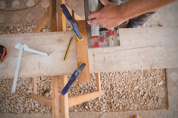 Carpenter using electrical saw on raw wood in his garage.
