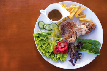 Pork steak is placed in a dish with fried potatoes and salads.