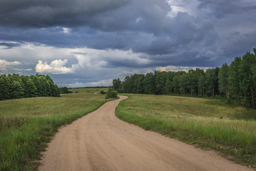 Fototapeta na wymiar Dust road among meadows in Masurian Lakeland region of Poland