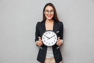 Smiling woman in eyeglasses holding clock and looking at camera