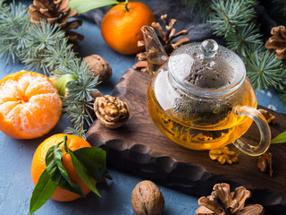 Winter tea in pot and tangerines with pine cones and fir tree branches