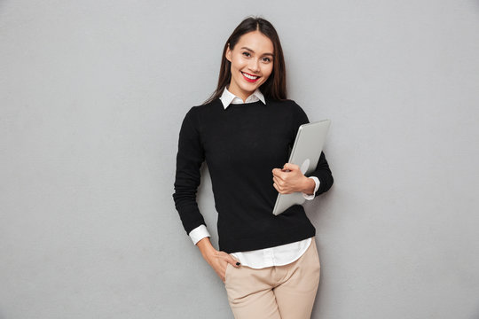 Smiling asian woman in business clothes holding laptop computer