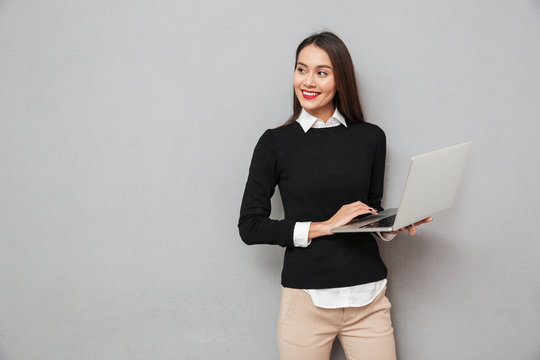 Pleased asian woman in business clothes holding laptop computer