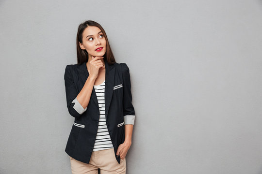 Pensive asian business woman with arm in pocket holding chin