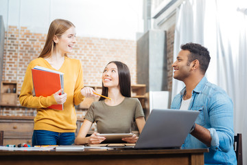 Rather good. Kind attentive cheerful students sitting at the table and looking at their cute smiling friend and feeling glad while studying with her