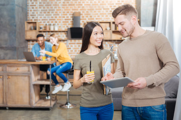 Fototapeta premium Convenient device. Cheerful friendly students standing together with folders in their hands and feeling glad while spending time together