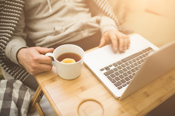Young man laying in bad with laptop and cup of tea.