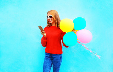 Fashion smiling woman is using smartphone with an air balloons on blue background