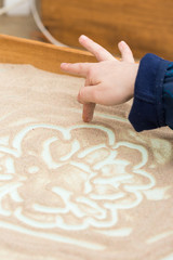 pedagogy, handcraft, childhood concept. close up of small arm of boy that has drawing classes, he uses sand creating curly lines on the white surface