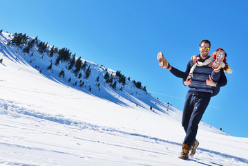 Young couple having fun on snow. Happy man at the mountain giving piggyback ride to his smiling girlfriend.