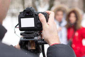 Fototapeta premium season, hobby, art work concept. close up of professional camera with blank screen in the arm of photographer on the background of two models that wear winter clothes