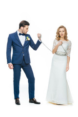 groom holding shocked young bride on chain isolated on white