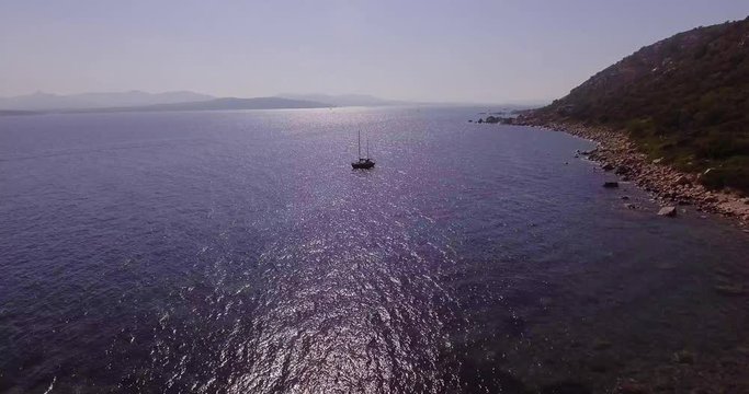 Aerial, a lonely sailing ship in backlight in a beautiful bay with crystalline water
