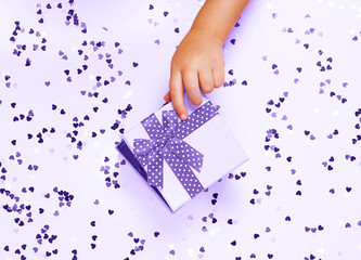 Child's hand opening gift box on pinh background with heart shaped confetti. Top view, flat lay. ultra violet style