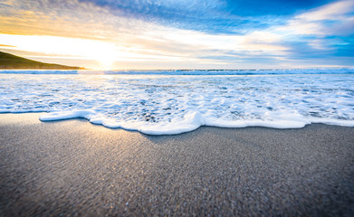 Small ocean sea waves on sandy beach with sunrise sunset.